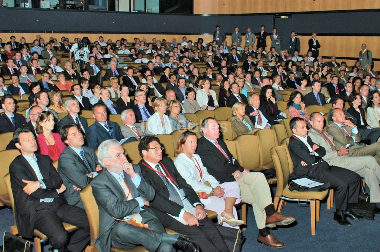 Salle comble avec un public attentif assis sur des rangées de sièges lors d'une conférence ou d'un événement professionnel.