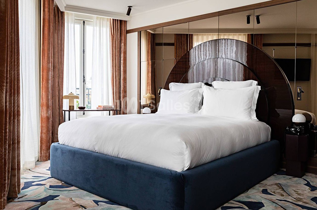 Lit double avec draps blancs dans une chambre élégante, décorée de rideaux marron, miroirs et tapis coloré.