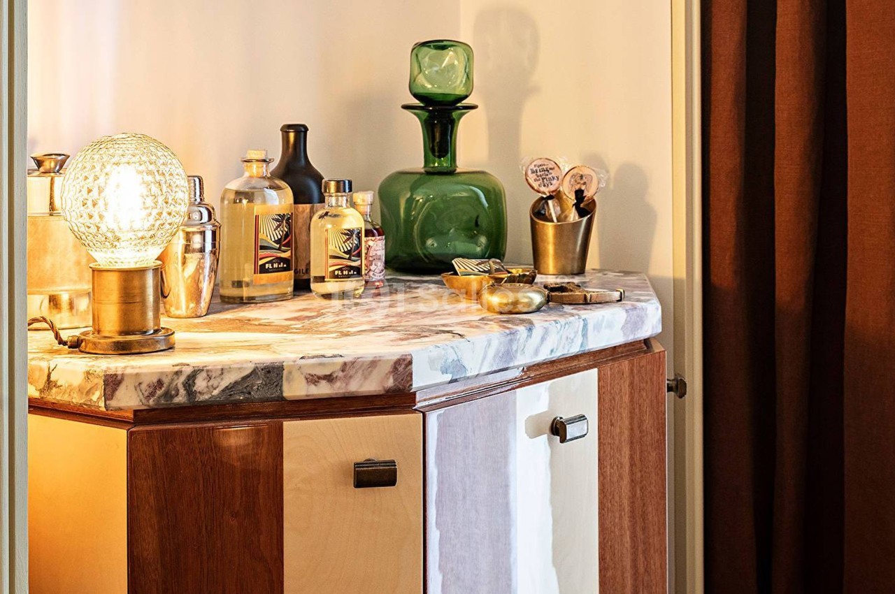 Meuble en bois avec plateau en marbre, décoré de bouteilles, objets vintage et une lampe en verre texturé.