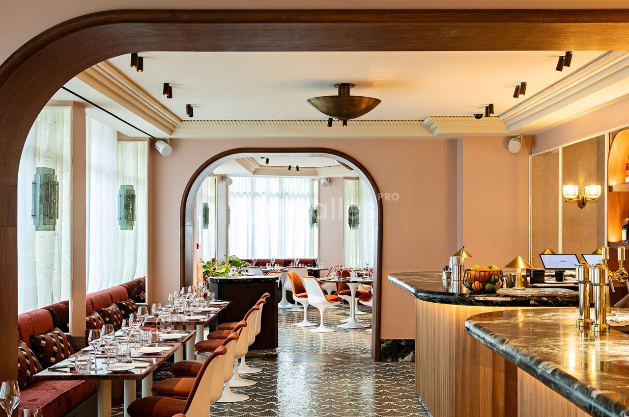 Salle de restaurant lumineuse avec tables dressées, bar en marbre et arches en bois dans un décor moderne.
