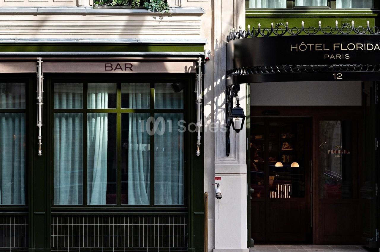 Façade d'un hôtel parisien avec une entrée en bois et un bar adjacent, fenêtres ornées de rideaux blancs.