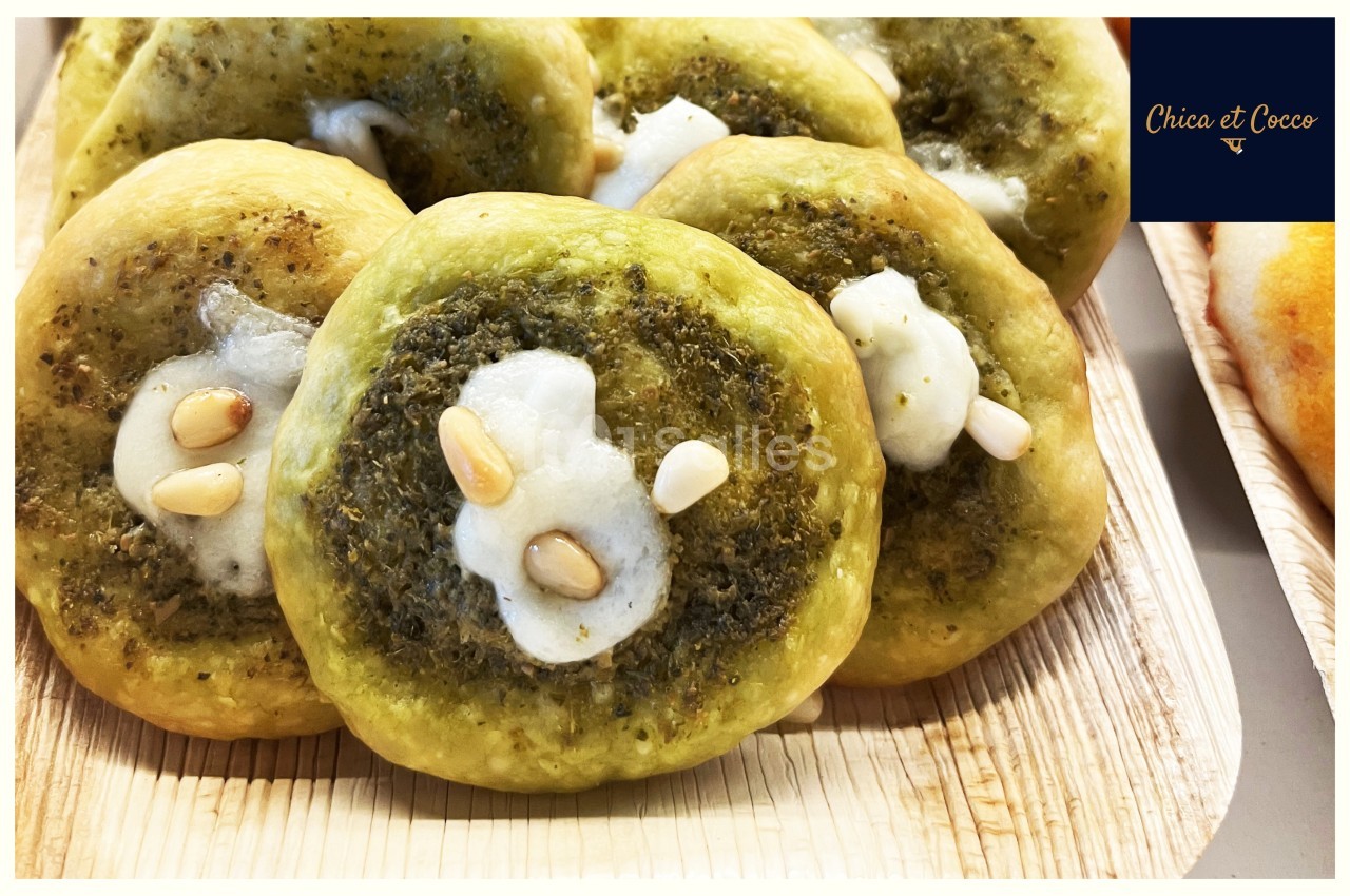 Petites pizzas garnies de zaatar, fromage fondu et pignons de pin, présentées sur un plateau en bois.