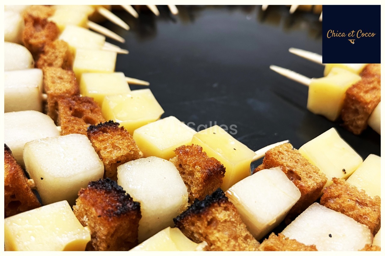 Brochettes apéritives composées de cubes de fromage et de pain grillé disposées en cercle sur un plateau noir.