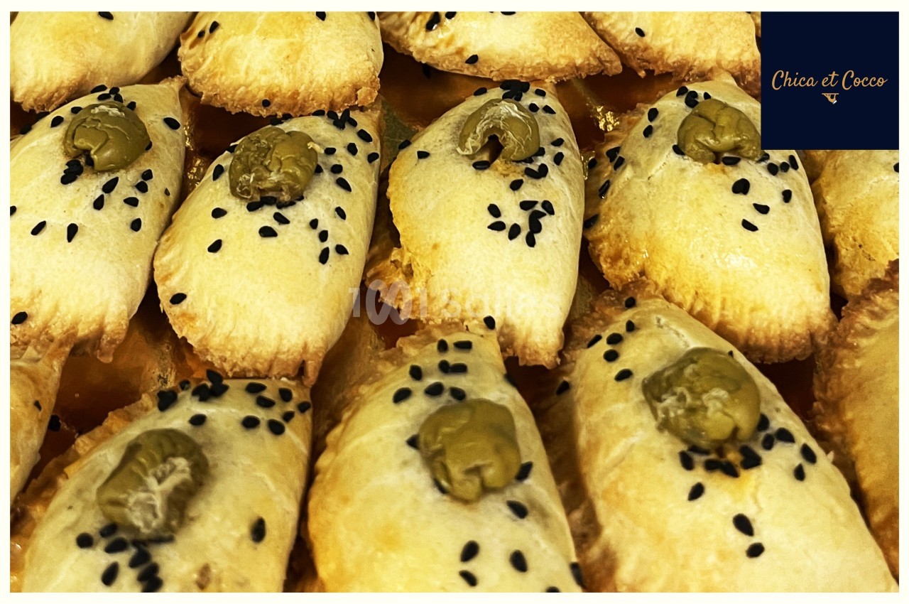 Assortiment de petits feuilletés dorés garnis d'olives vertes et parsemés de graines de sésame noires.
