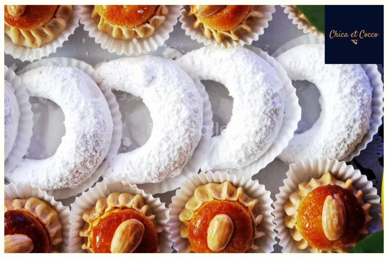 Assortiment de pâtisseries orientales, incluant des cornes de gazelle saupoudrées de sucre glace et des gâteaux aux amandes.