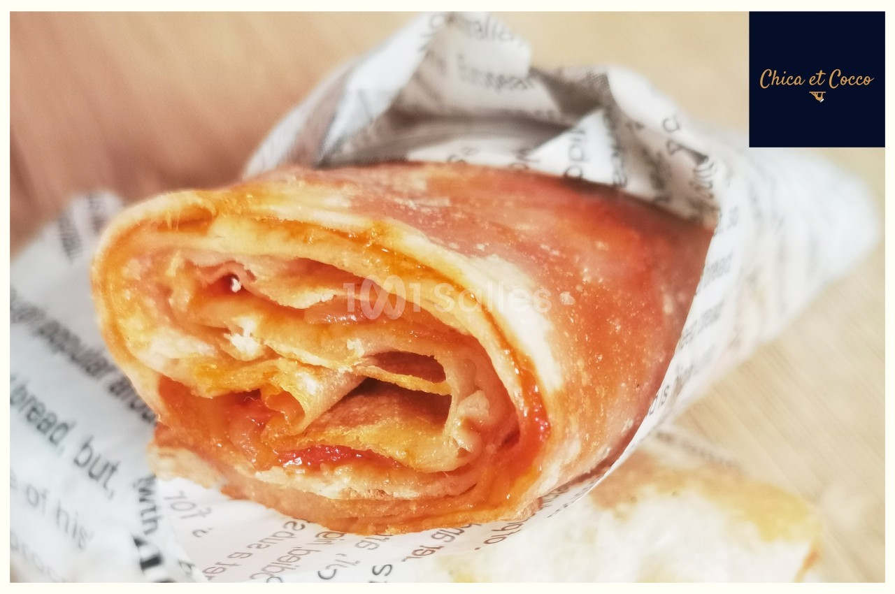 Crêpe roulée garnie de confiture, enveloppée dans un papier imprimé, posée sur une surface en bois.