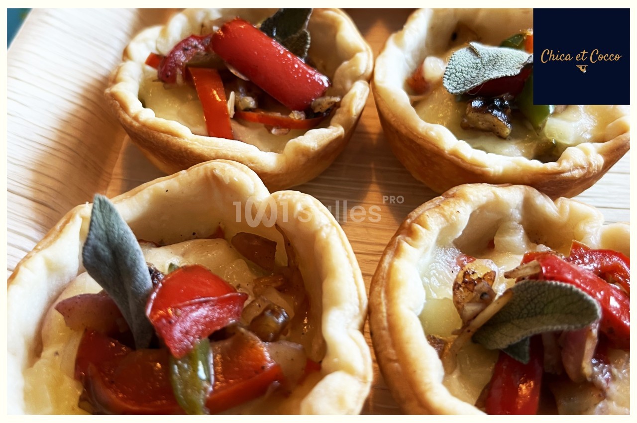 Quatre tartelettes garnies de légumes grillés et décorées de feuilles de sauge, présentées sur une assiette en bois.