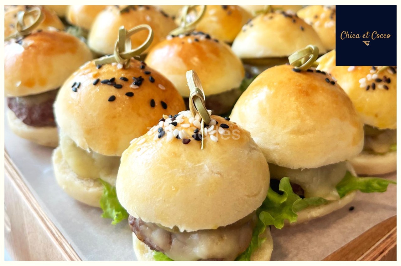 Plateau de mini-burgers garnis de salade, fromage et steak, présentés avec des piques en bois.