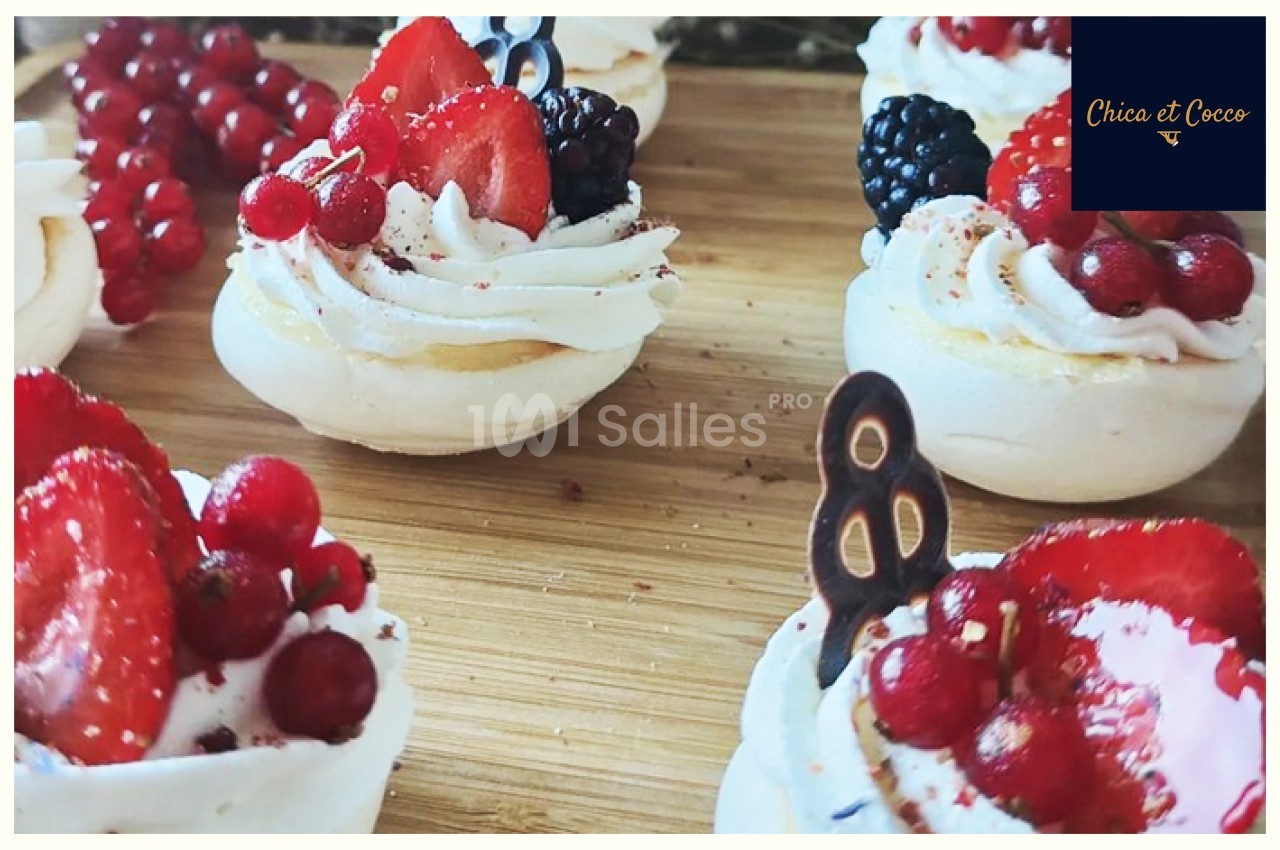 Petites meringues garnies de crème fouettée, fraises, groseilles et mûres, présentées sur une planche en bois.