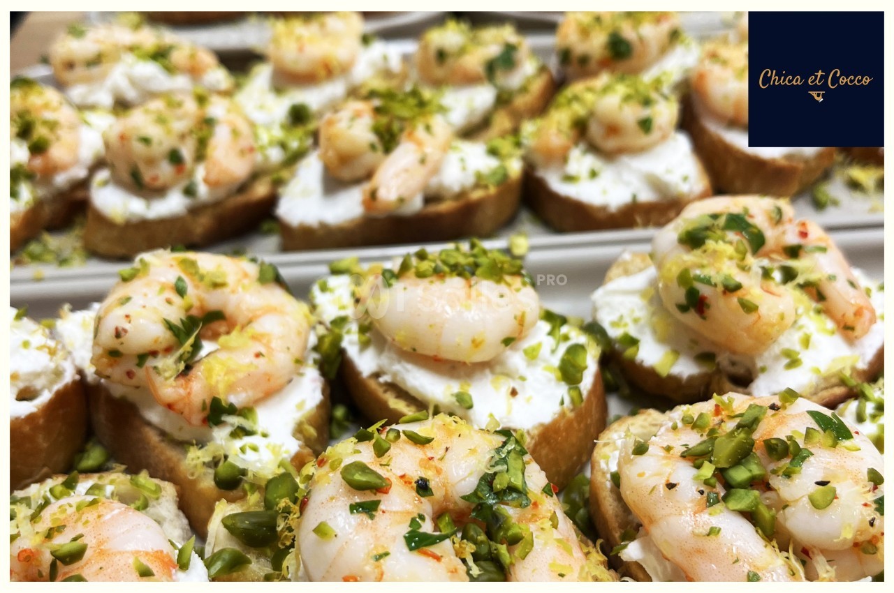 Tranches de pain garnies de fromage frais, crevettes et éclats de pistaches, présentées sur un plateau.