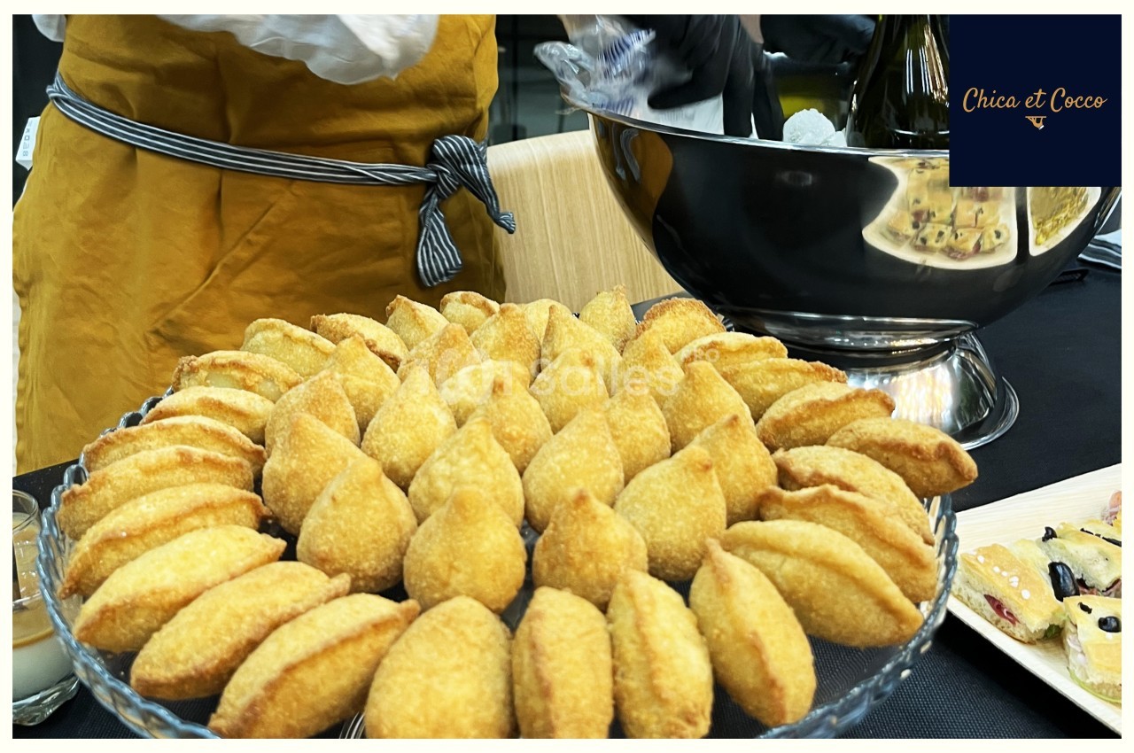 Assiette garnie de beignets dorés en forme de demi-lune, présentée sur une table avec une coupe en arrière-plan.