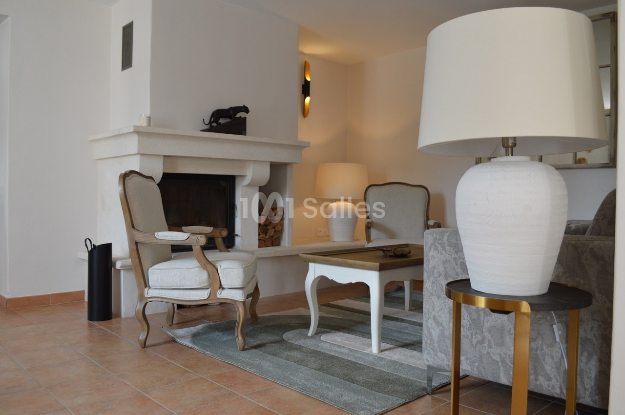 Salon lumineux avec cheminée, fauteuils en bois, table basse blanche, tapis rayé et lampes sur des tables d'appoint.