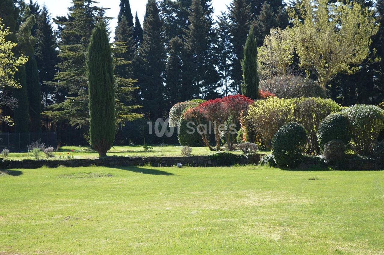 Jardin avec pelouse, arbustes taillés, arbres variés et haies colorées sous un ciel dégagé.