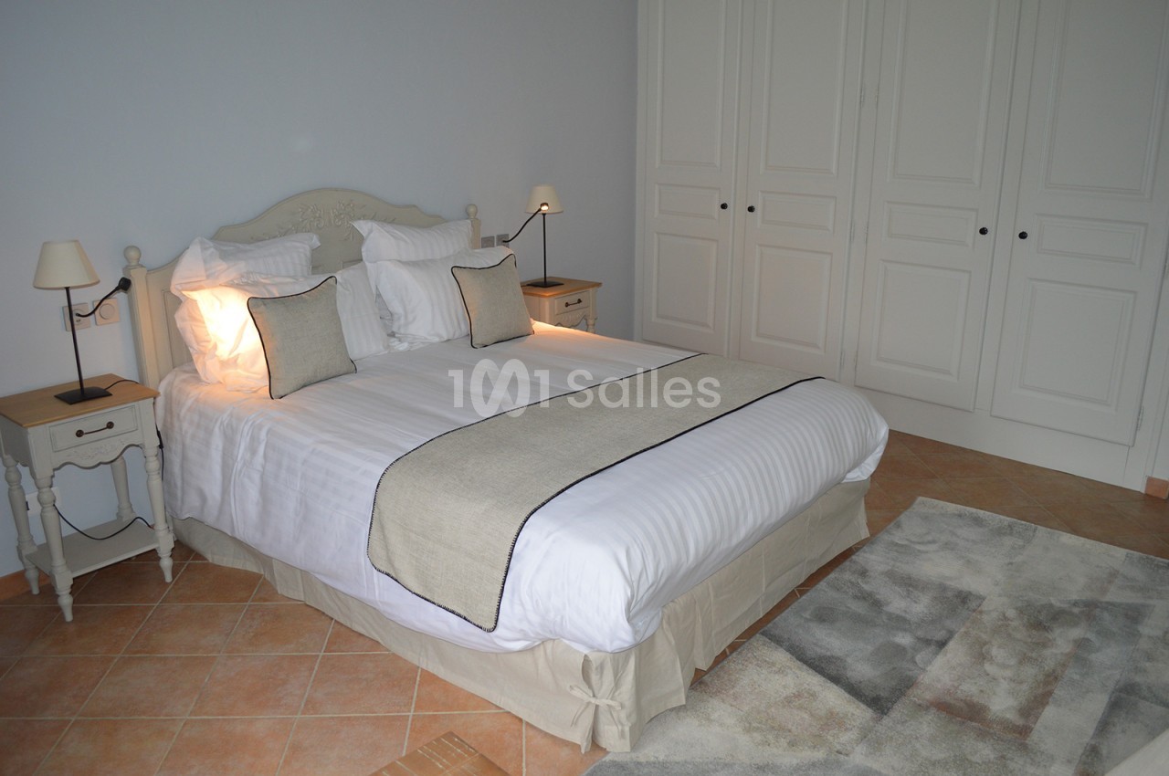 Chambre avec lit double, linge blanc, coussins beiges, tables de chevet avec lampes et armoire blanche en arrière-plan.