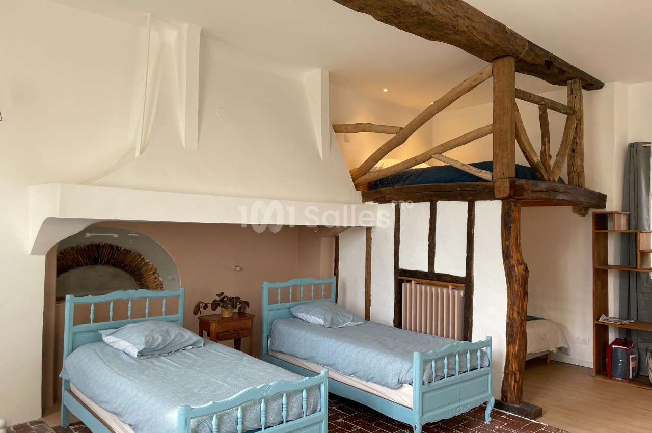 Chambre avec deux lits simples, mezzanine en bois, poutres apparentes et sol en carrelage ancien.