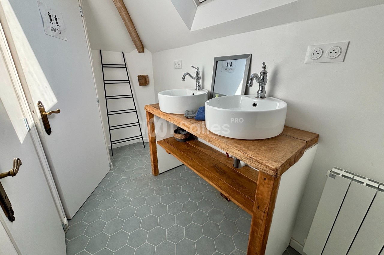 Salle de bain lumineuse avec deux vasques blanches sur un meuble en bois, miroir et carrelage hexagonal gris.