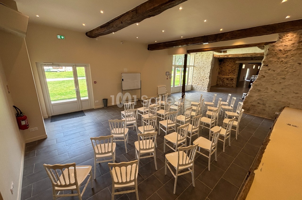 Salle de réunion lumineuse avec des chaises blanches disposées face à un tableau blanc, murs en pierre apparente.