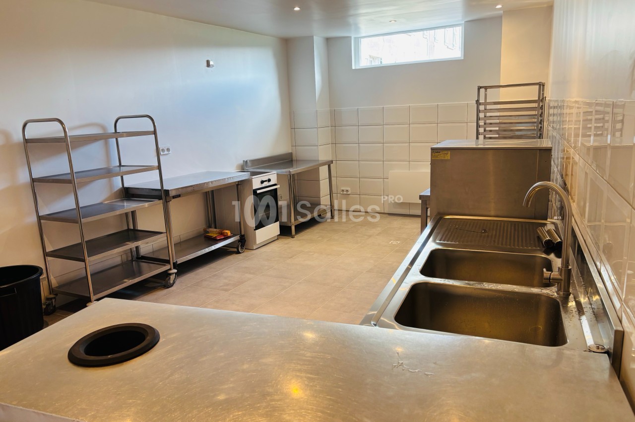 Cuisine professionnelle avec plans de travail en inox, éviers, étagères métalliques et éclairage naturel.