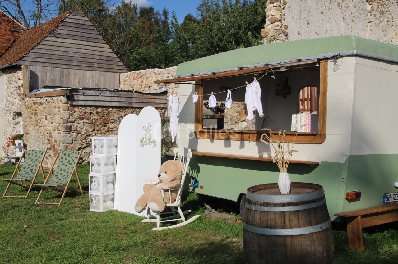 Une caravane aménagée en boutique avec des articles pour bébé, entourée de décorations champêtres et de chaises longues.