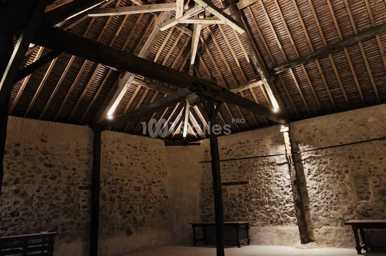 Charpente en bois apparente dans une pièce aux murs en pierre, éclairée par une lumière tamisée.