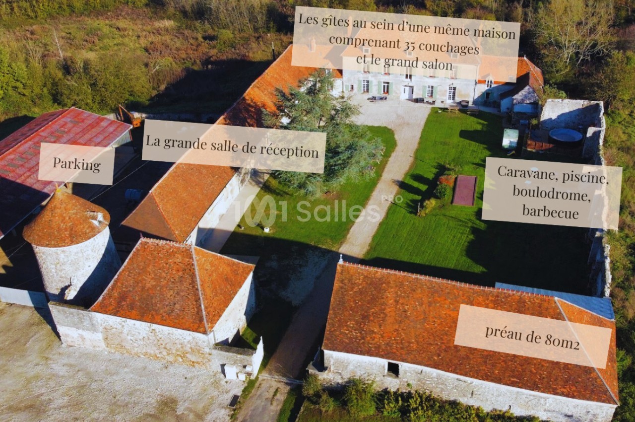 Vue aérienne d'un domaine avec bâtiments en pierre, parking, préau, piscine, caravane et espaces extérieurs aménagés.