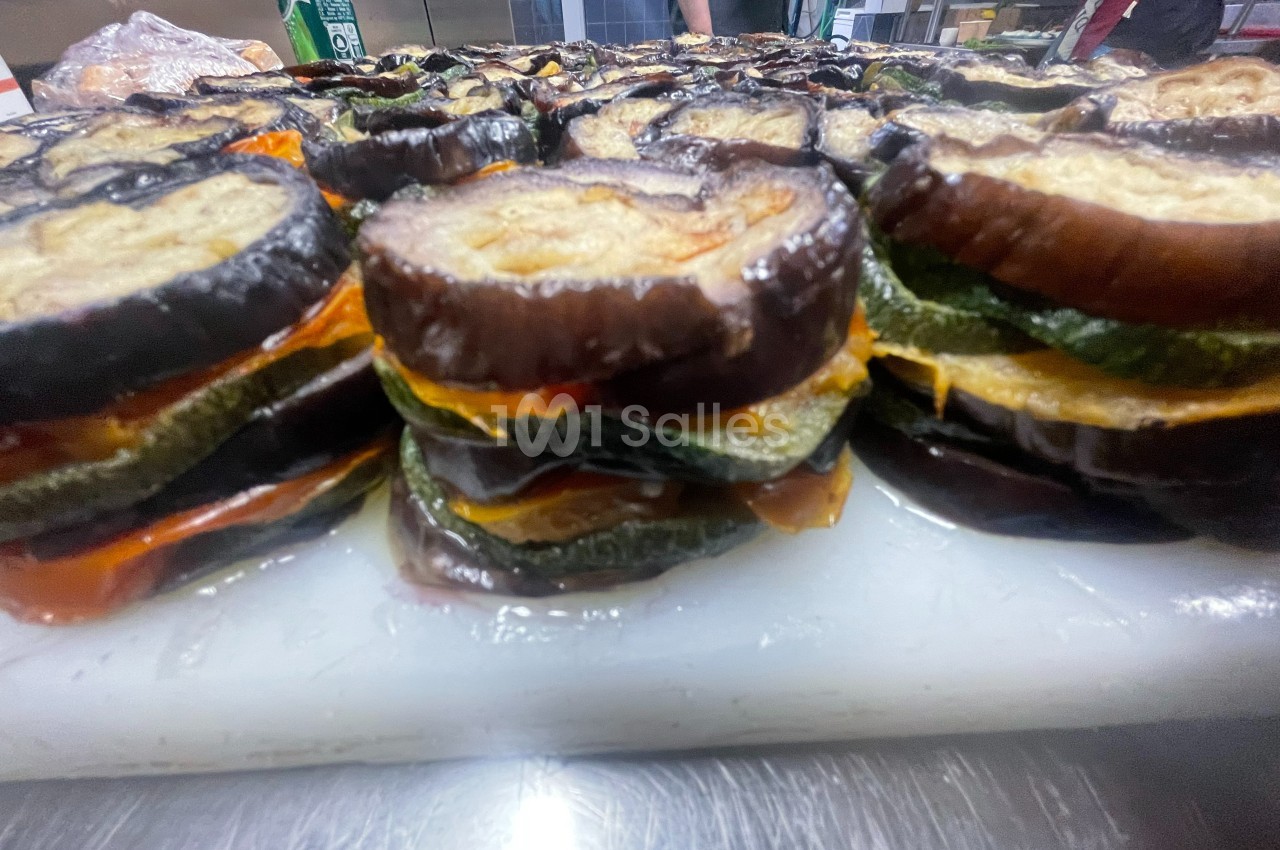 Tranches d'aubergines, courgettes et poivrons superposées, disposées sur un plan de travail en cuisine.
