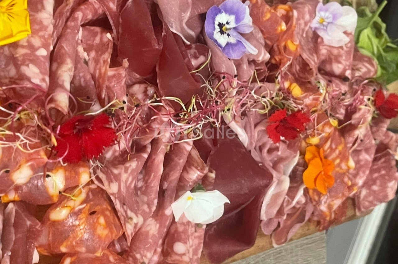Plateau de charcuterie variée décoré de fleurs comestibles colorées et de pousses, présenté sur une planche en bois.