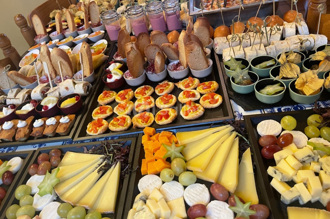 Buffet varié avec fromages, fruits, verrines, pains, tartes et amuse-bouches disposés sur plusieurs plateaux.
