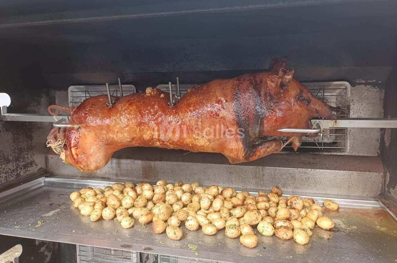 Cochon entier rôti à la broche dans un four, accompagné de pommes de terre dorées disposées en dessous.
