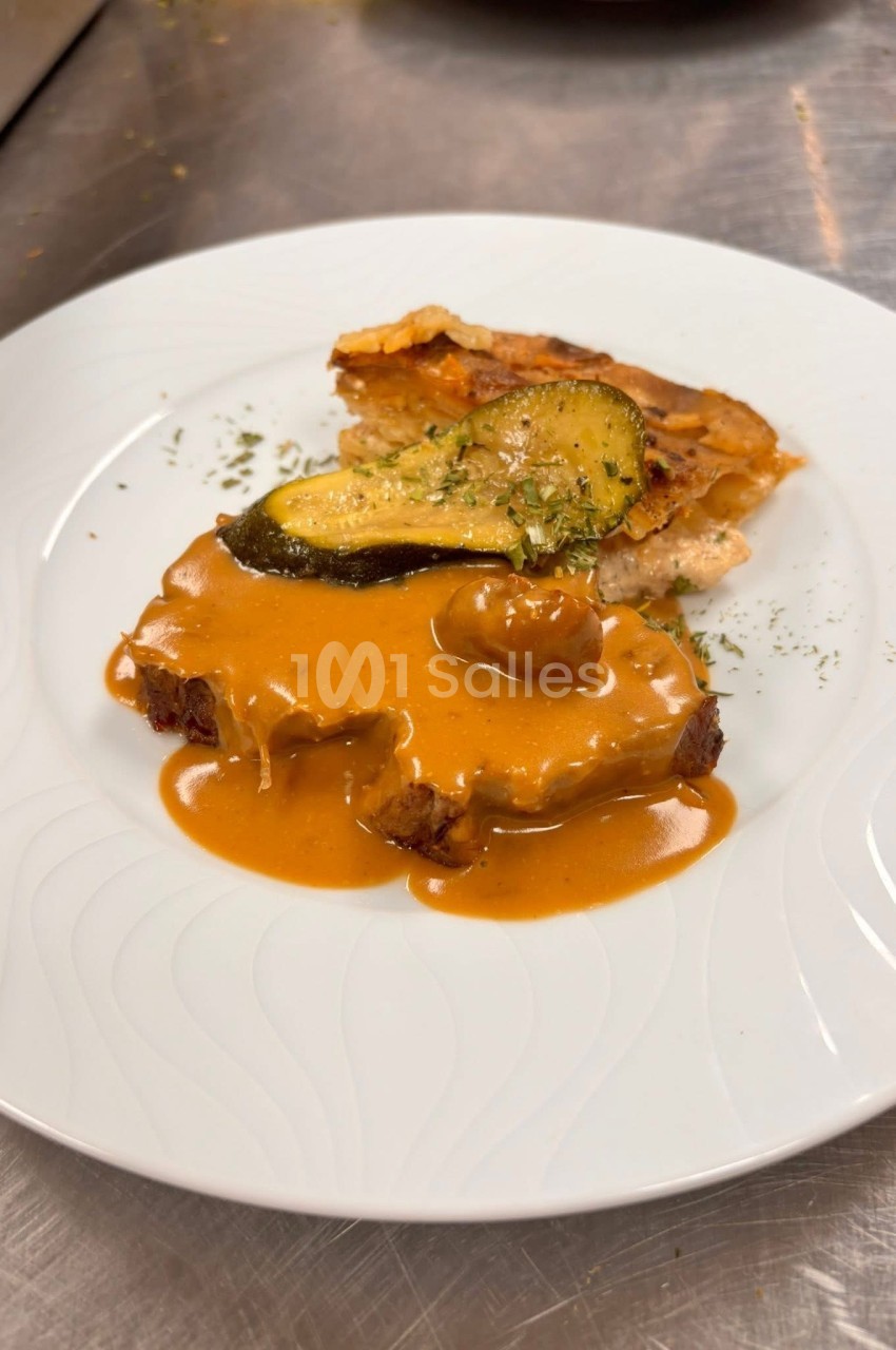 Assiette contenant une viande nappée de sauce brune, accompagnée de gratin et d'une tranche de courgette grillée.