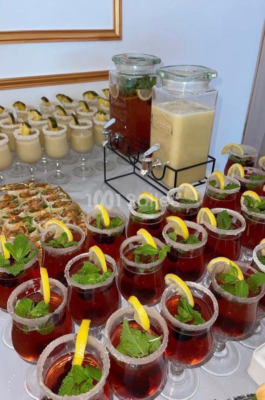 Buffet avec cocktails rouges garnis de citron et menthe, verrines, roulés apéritifs et boissons en distributeurs.