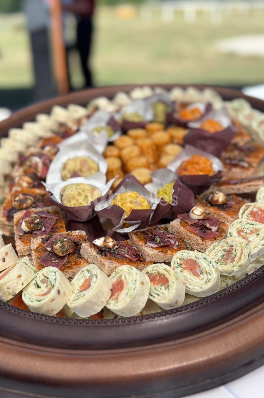 Plateau de bouchées apéritives variées comprenant wraps, toasts garnis et boulettes, présenté sur un plat en bois.