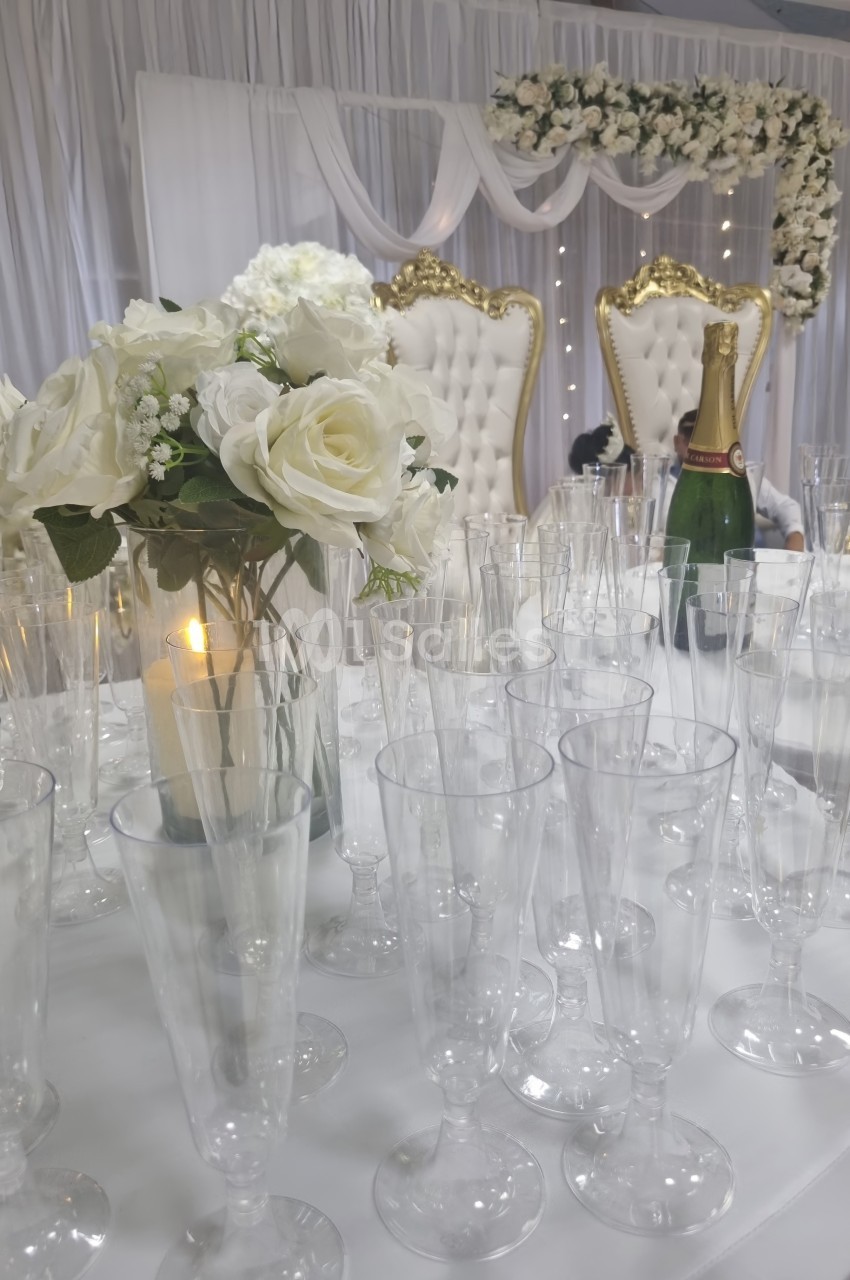 Table décorée avec des flûtes en verre, un bouquet de fleurs blanches, une bougie et des fauteuils ornés en arrière-plan.