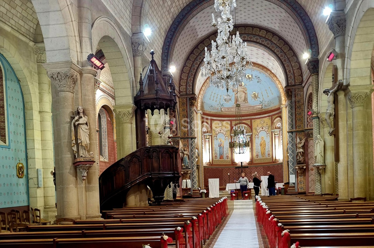 Intérieur d'une église avec bancs en bois, chaire sculptée, lustre central et fresques ornant le chœur.