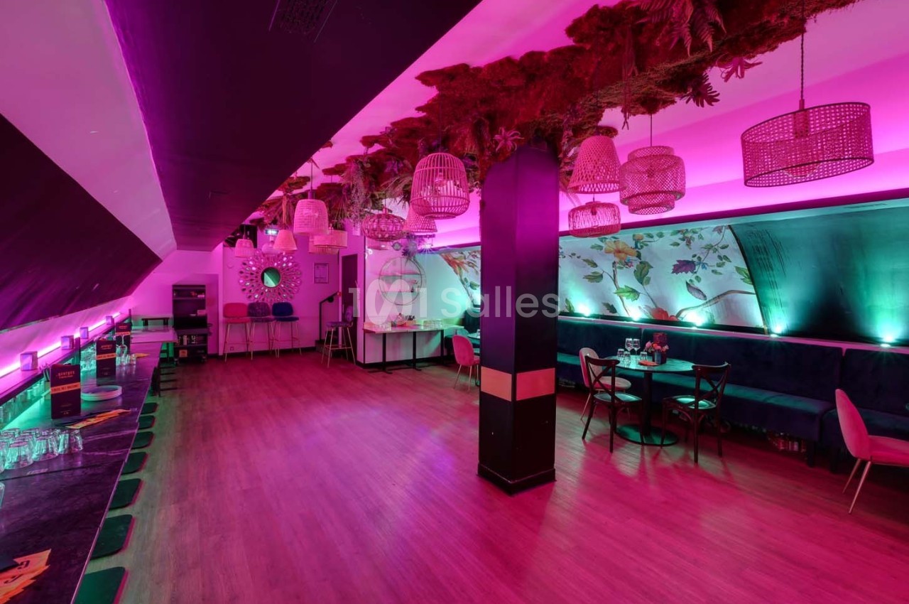 Salle moderne avec éclairage rose, tables et chaises, décorations suspendues et ambiance chaleureuse.