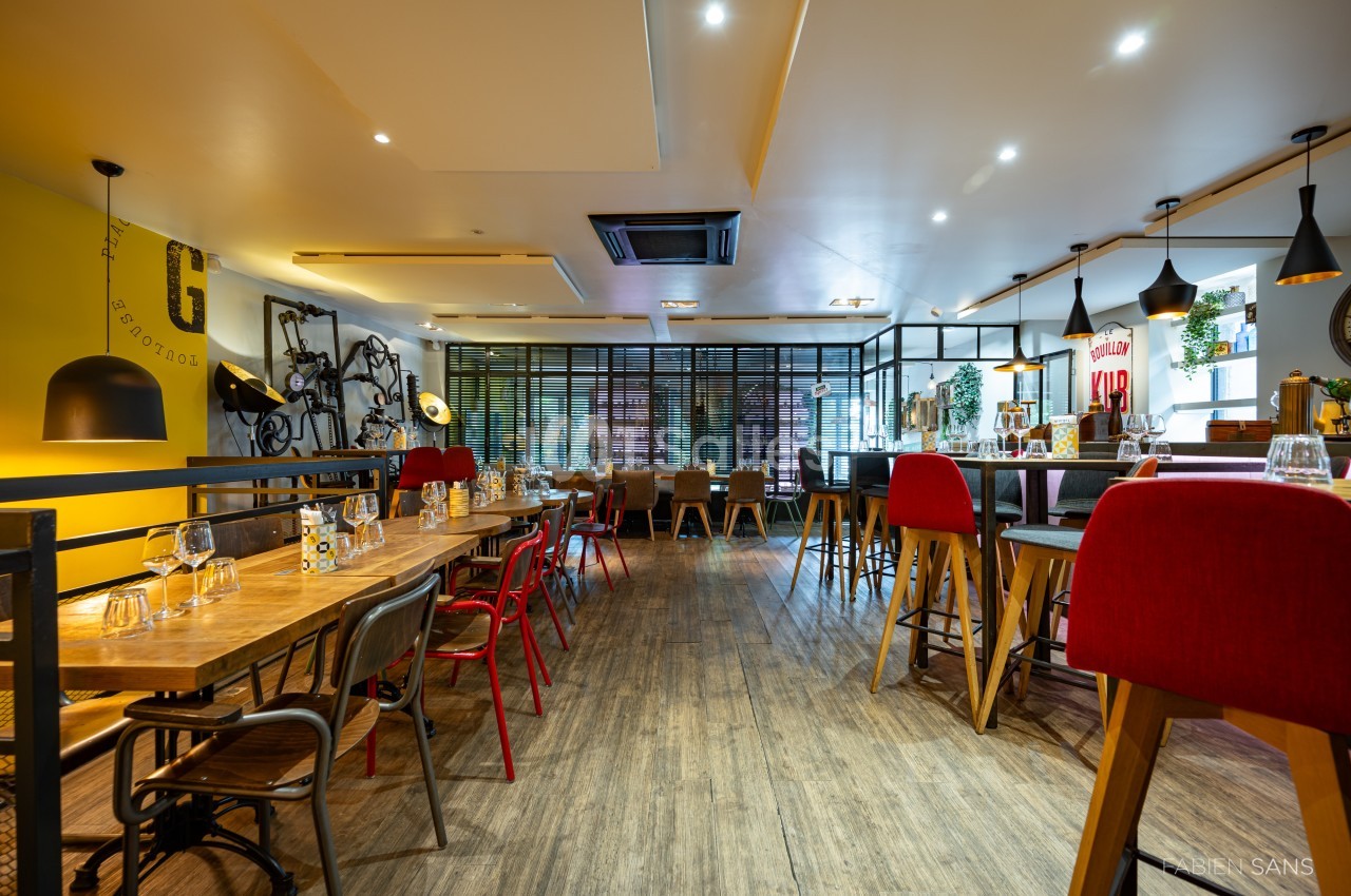 Salle de restaurant moderne avec tables en bois, chaises colorées et décoration murale industrielle.