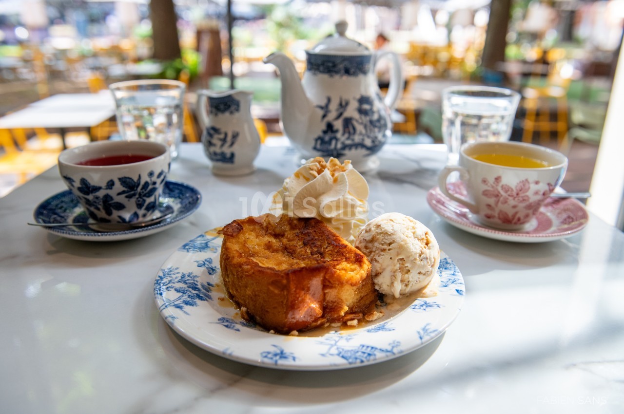 Assiette de pain perdu avec glace et chantilly, accompagnée de thé et café sur une table en terrasse.