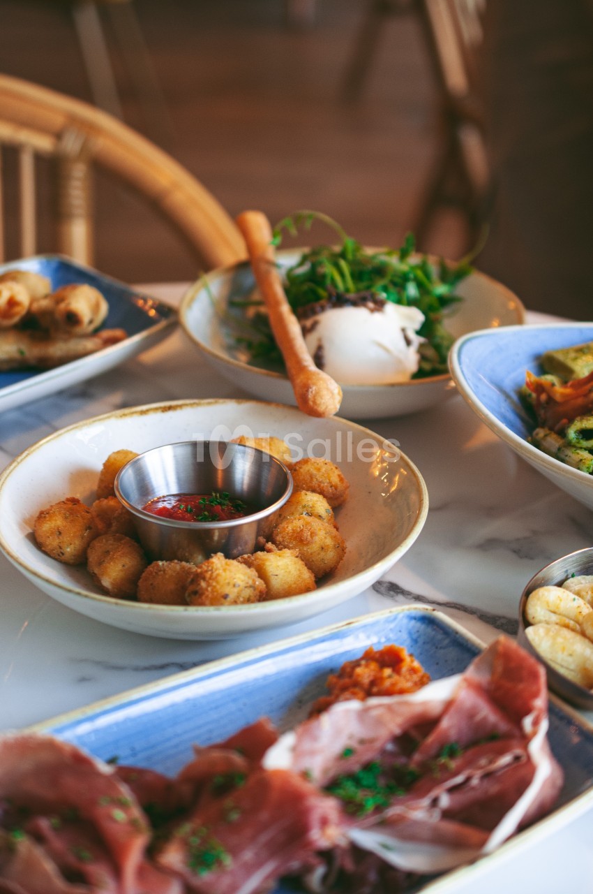 Assortiment de plats italiens sur une table, incluant burrata, charcuterie, croquettes et légumes grillés.
