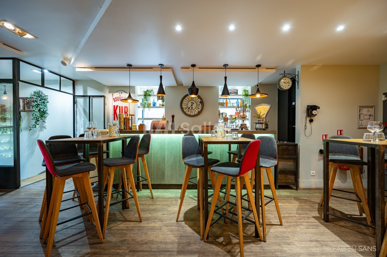 Salle de restaurant moderne avec tables hautes, chaises colorées, éclairage chaleureux et décorations murales.