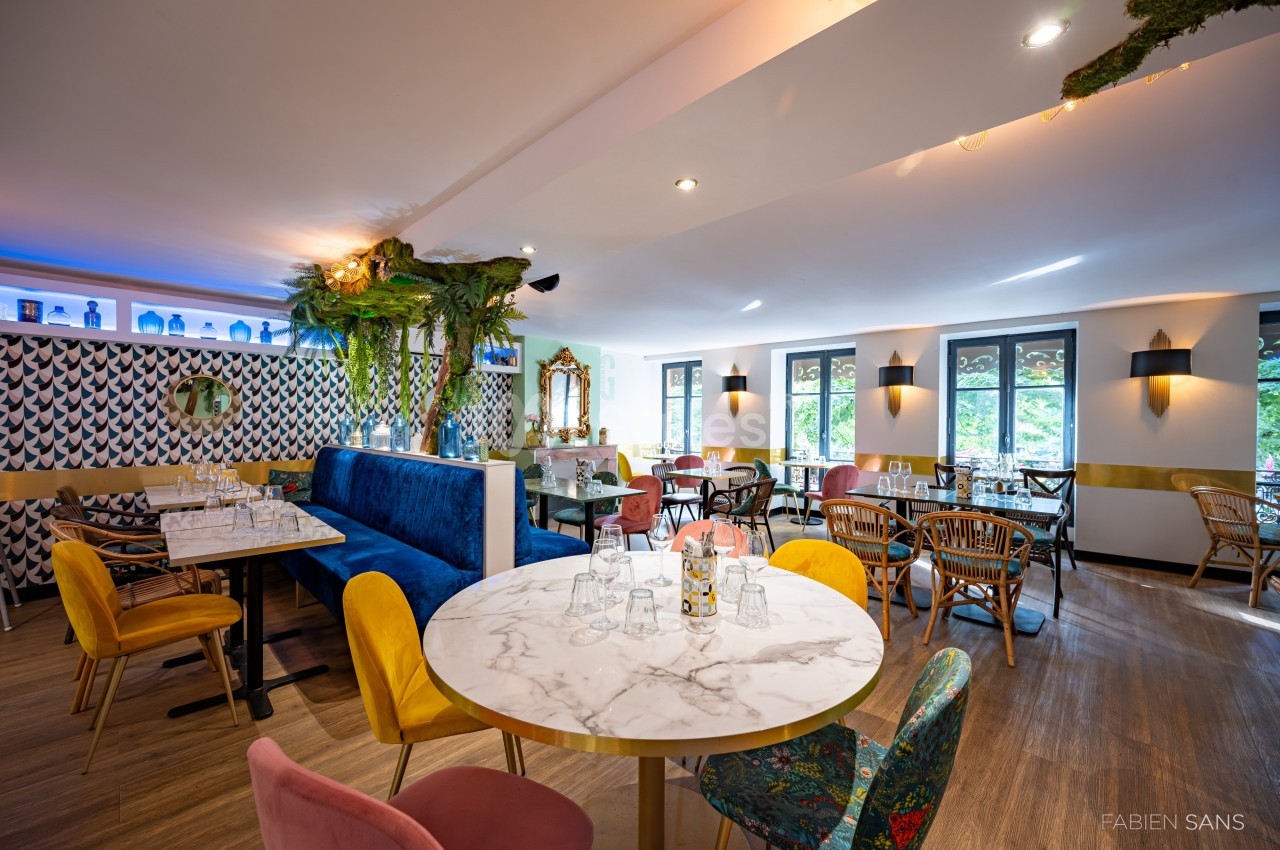 Salle de restaurant lumineuse avec tables en marbre, chaises colorées et décoration végétale.
