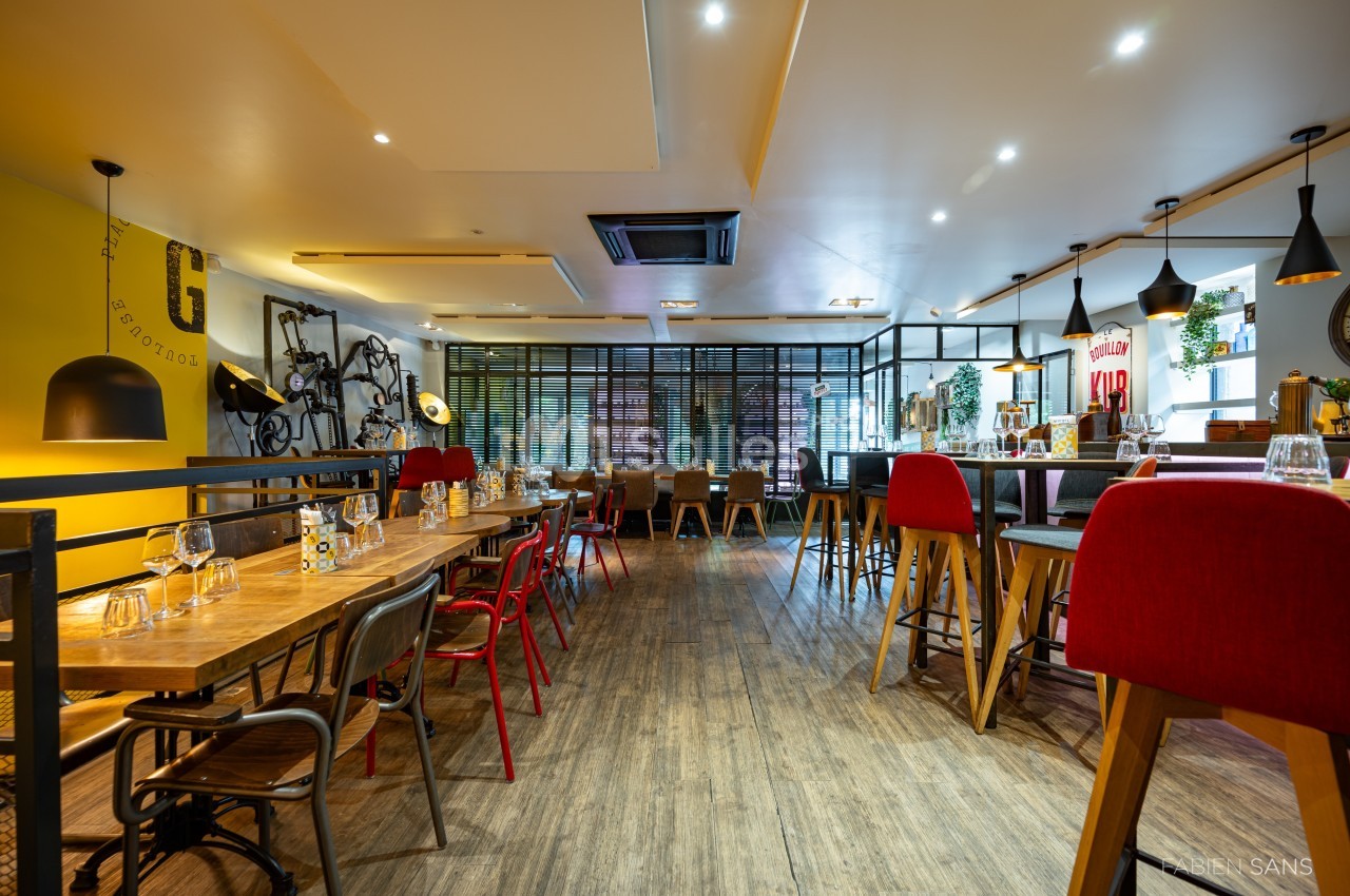 Salle de restaurant moderne avec tables en bois, chaises colorées et décoration murale industrielle.