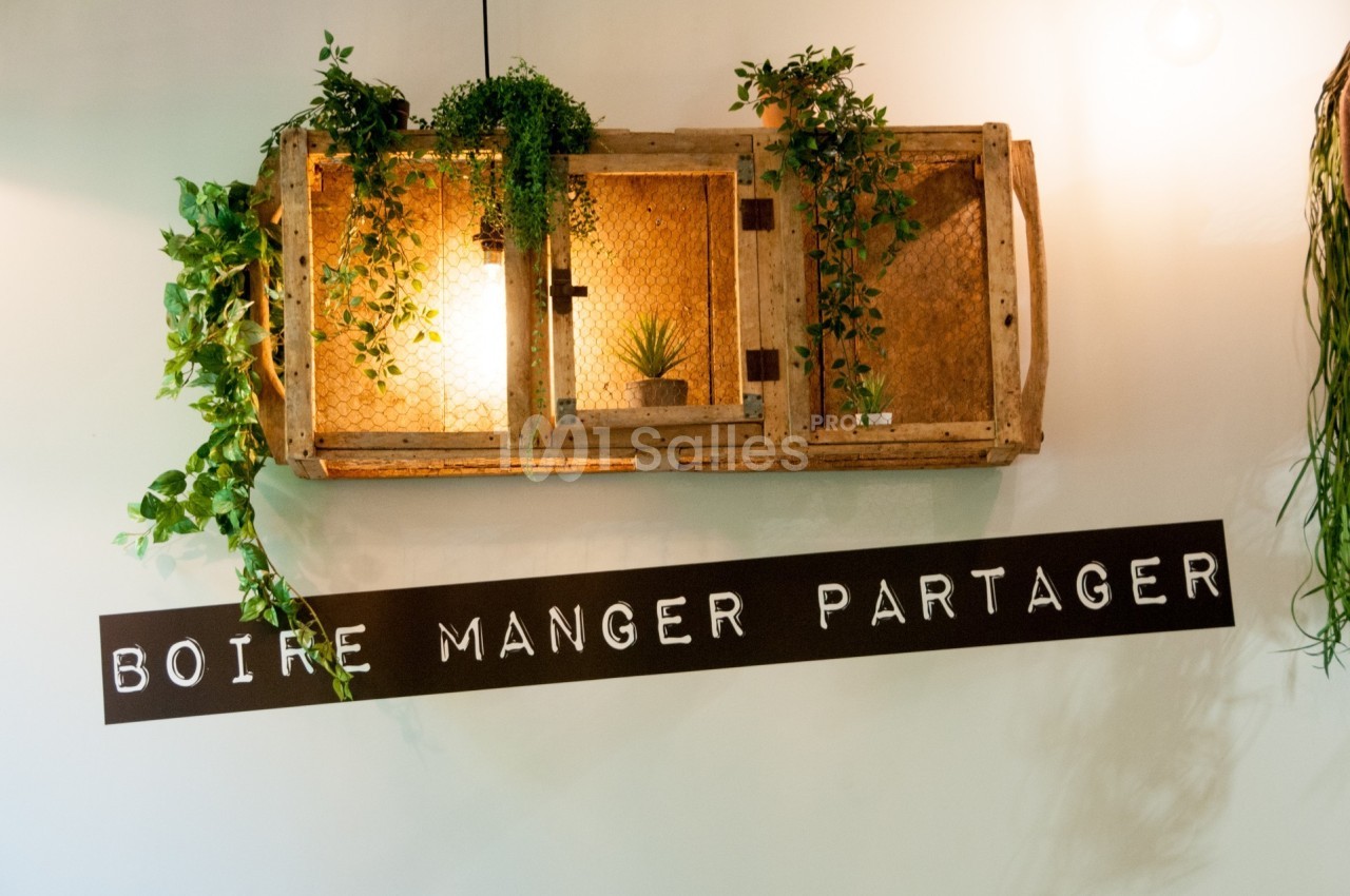 Étagère murale en bois décorée de plantes, éclairée par une lumière douce, avec l'inscription ’Boire Manger Partager’.