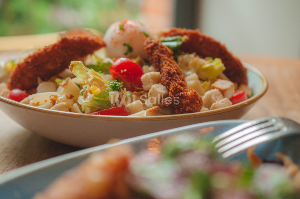 Salade composée avec morceaux de poulet pané, légumes frais, croûtons et œuf, servie dans un bol en céramique.