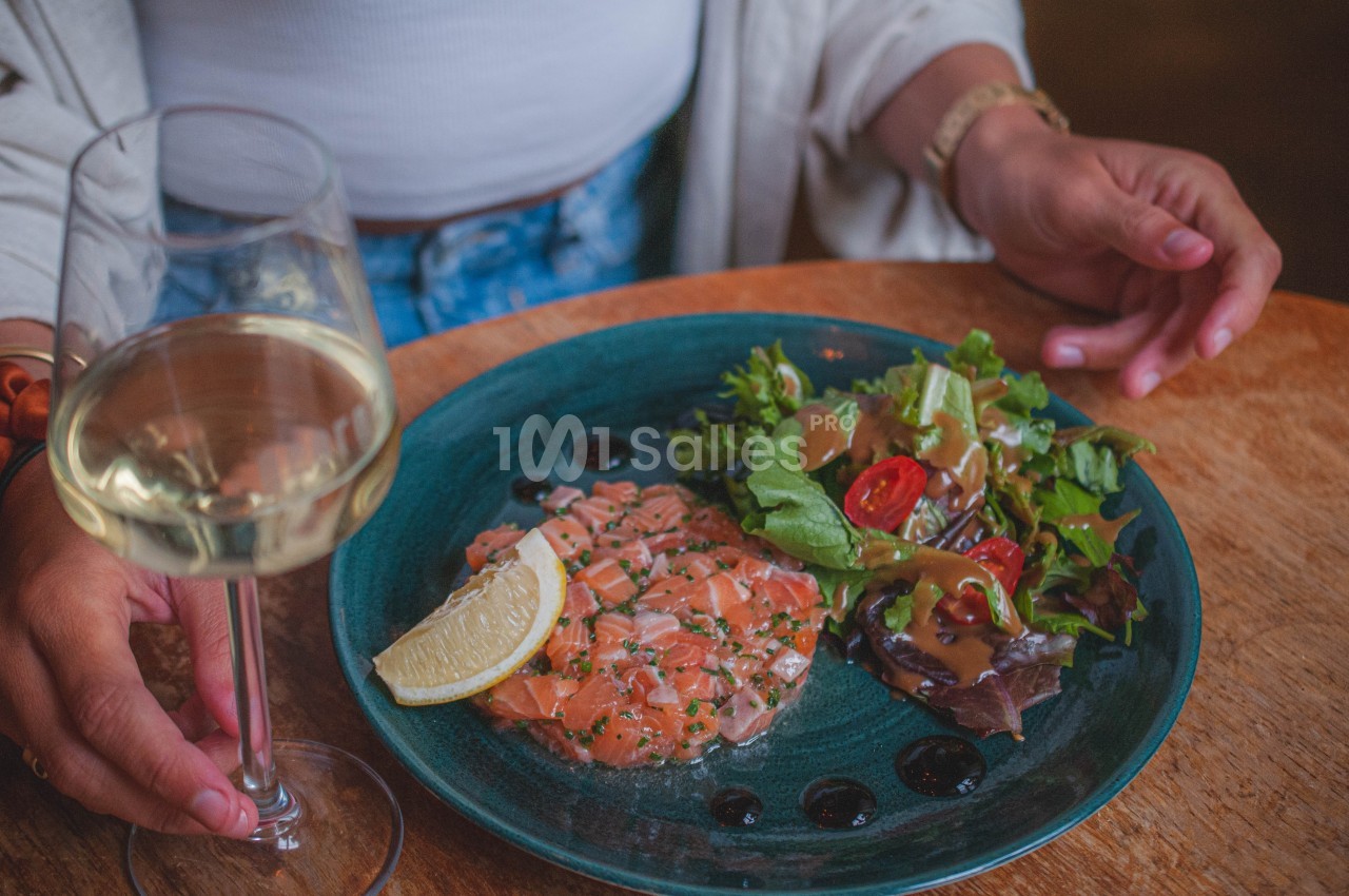 Assiette de tartare de saumon avec citron, salade verte et sauce, accompagnée d'un verre de vin blanc.