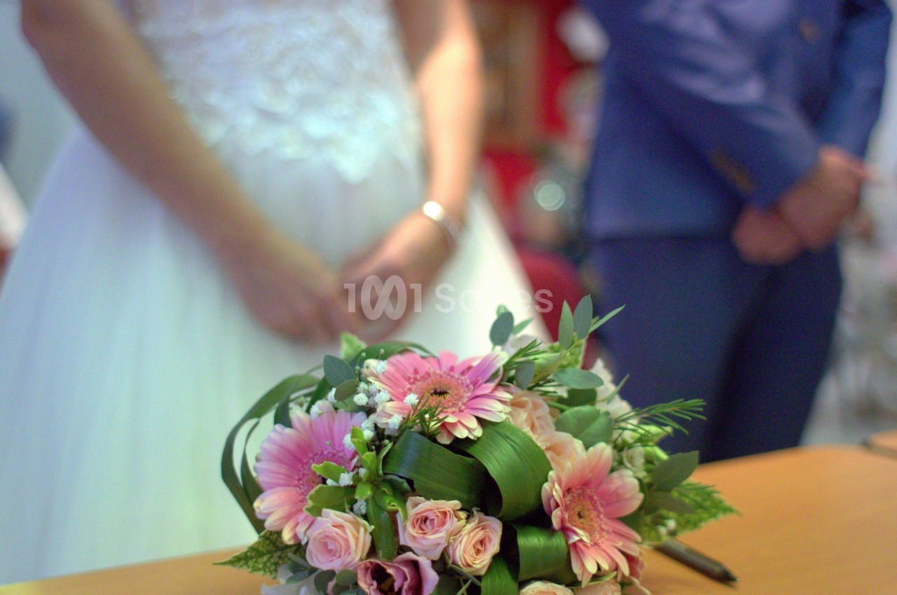Un bouquet de fleurs posé sur une table devant une mariée en robe blanche et un homme en costume bleu.