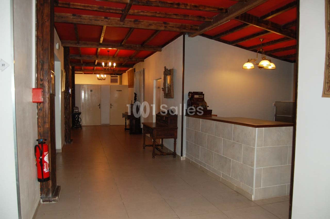 Couloir intérieur avec plafond en bois, murs blancs, comptoir à droite et porte au fond.