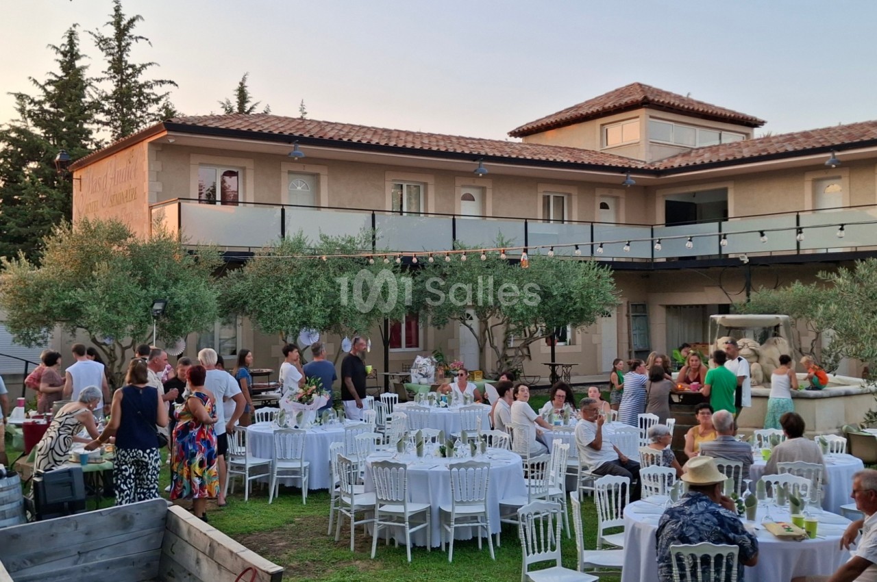 Groupe de personnes réunies dans un jardin avec tables dressées, devant une grande maison au crépuscule.