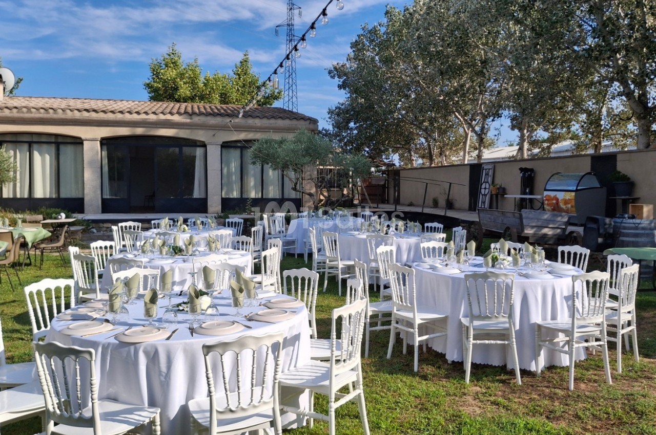 Tables rondes dressées avec nappes blanches et chaises, disposées dans un jardin pour un événement en plein air.