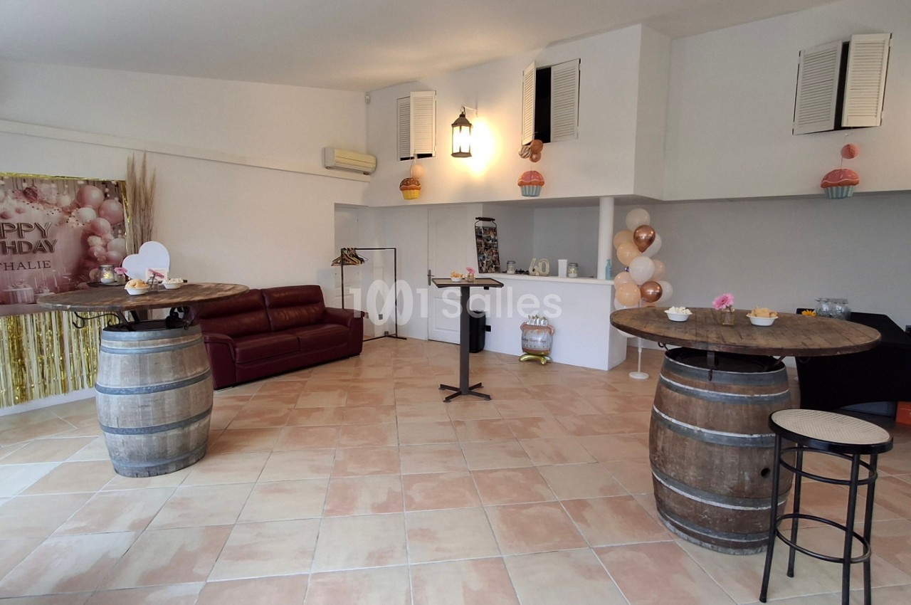 Salle décorée pour un anniversaire avec ballons, guirlande dorée, tonneaux en tables et canapé en arrière-plan.
