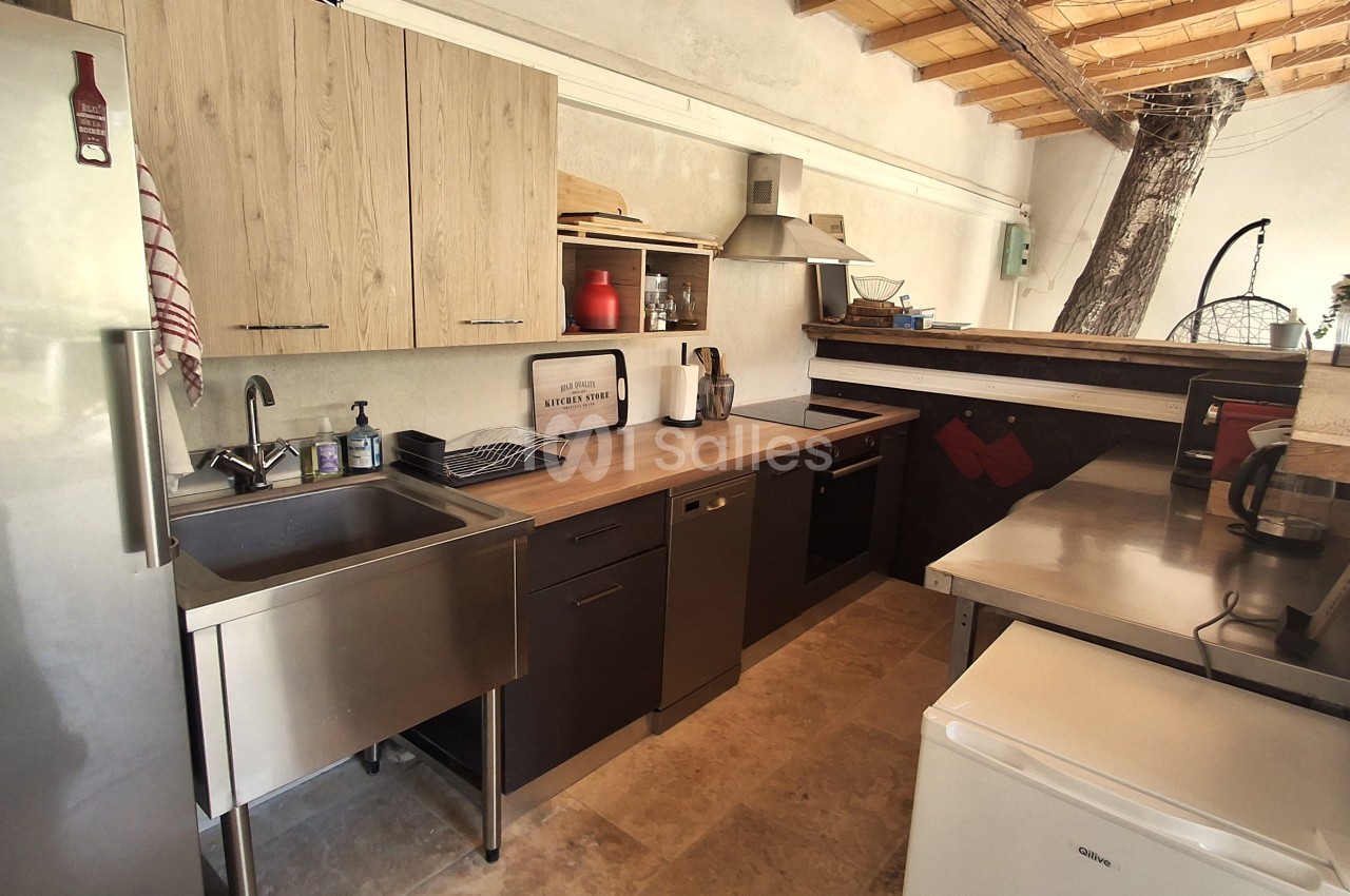 Cuisine moderne avec plan de travail en bois, évier en inox, électroménagers intégrés et plafond en bois apparent.